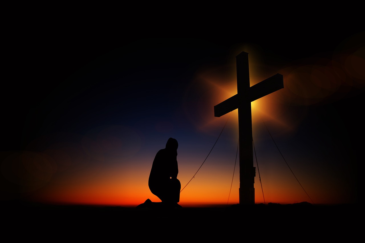 Cross silhouette at sunset with the person kneeling symbolizing salvation through Jesus