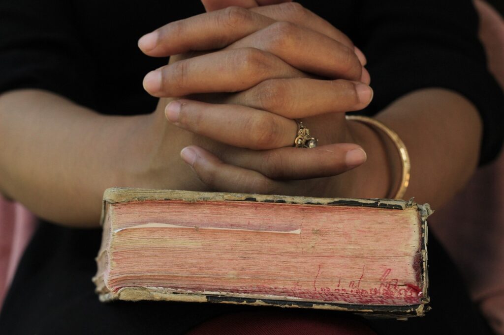 Open Bible and hands lifted in prayer symbolizing confession and belief