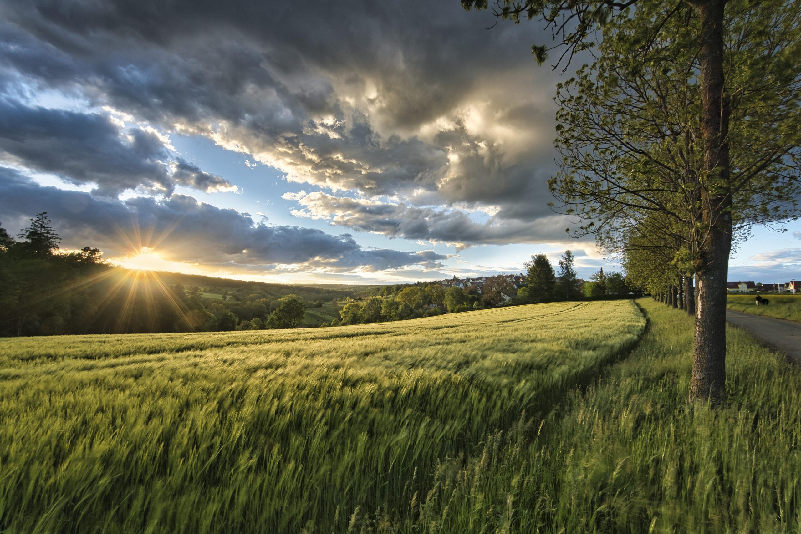 Sunlight breaking through dark clouds over a peaceful countryside, symbolizing God's blessings, hope, and His faithful presence in every season.