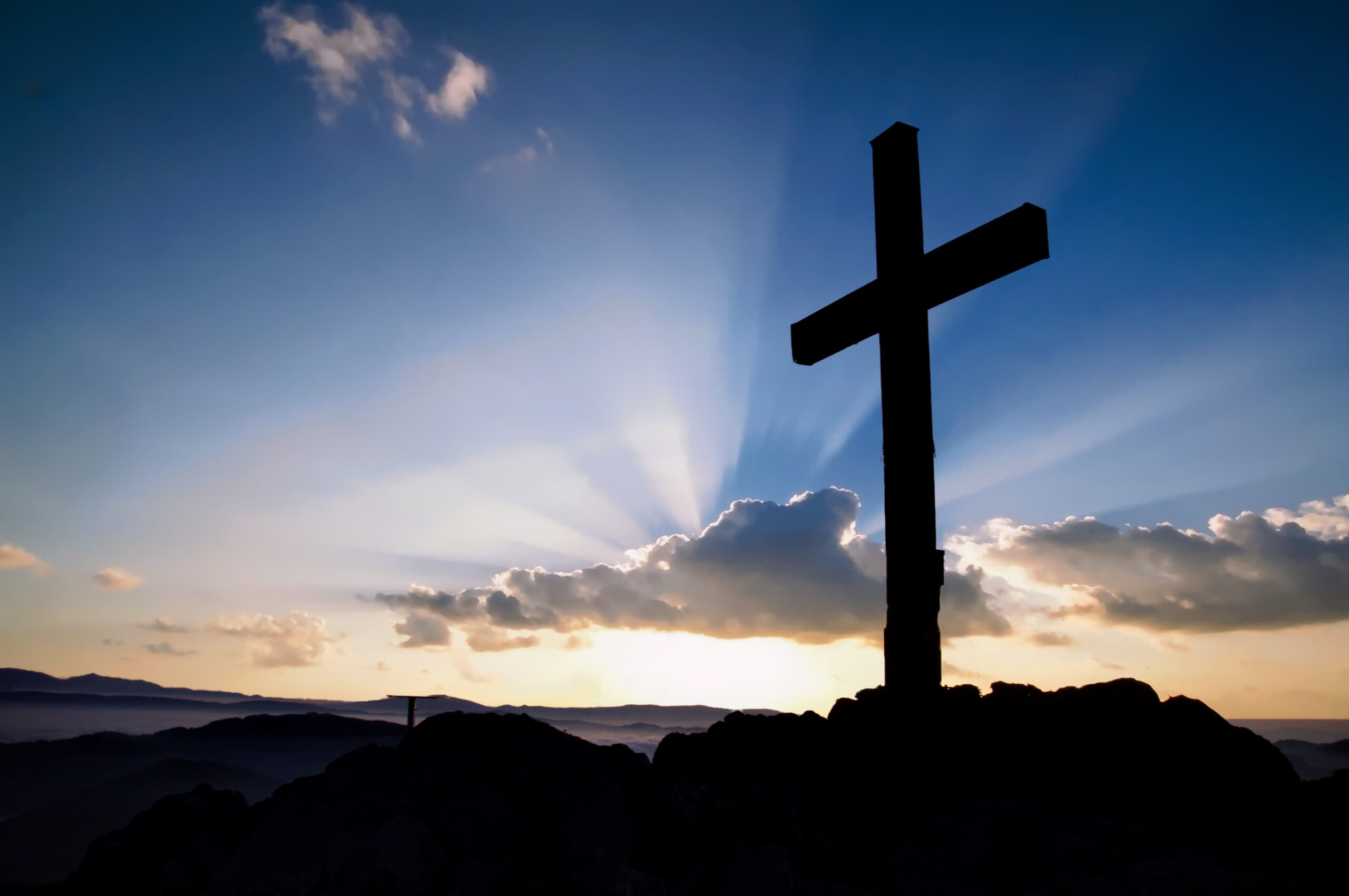 Wooden cross standing on a hill at sunrise, symbolizing God's love revealed through Jesus Christ in John 3:16.