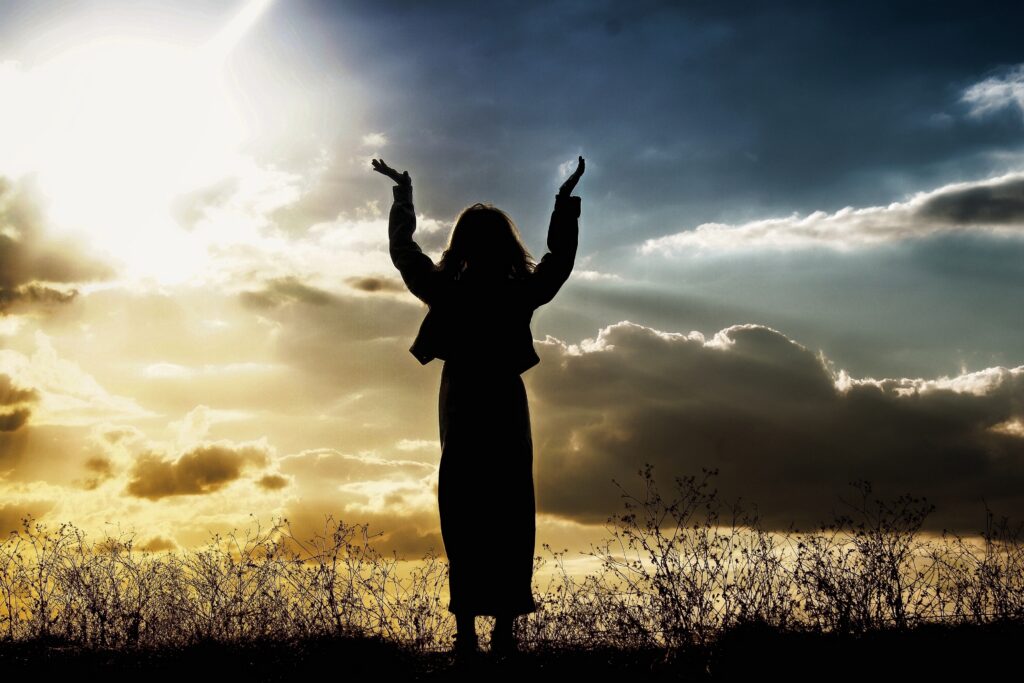 Hands raised in worship at sunrise through clouds, symbolizing God's unconditional love
