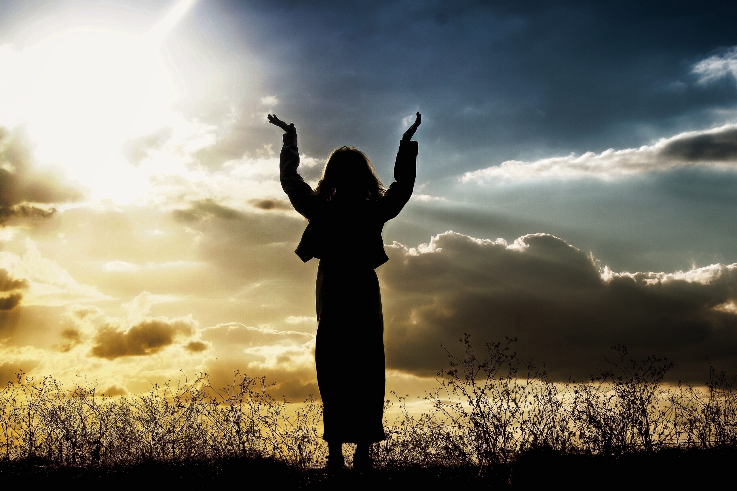 Hands raised in worship at sunrise through clouds, symbolizing God's unconditional love