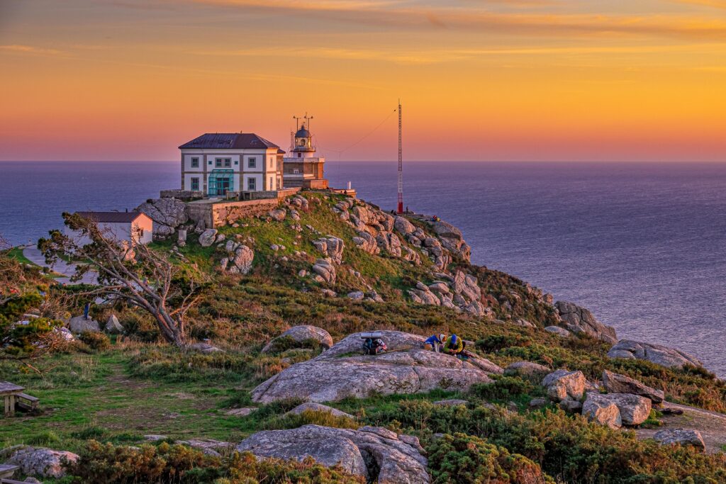 House built on rocky cliff by the sea bathed in sunlight beneath a stormy sky, symbolizing a life built on Jesus Christ