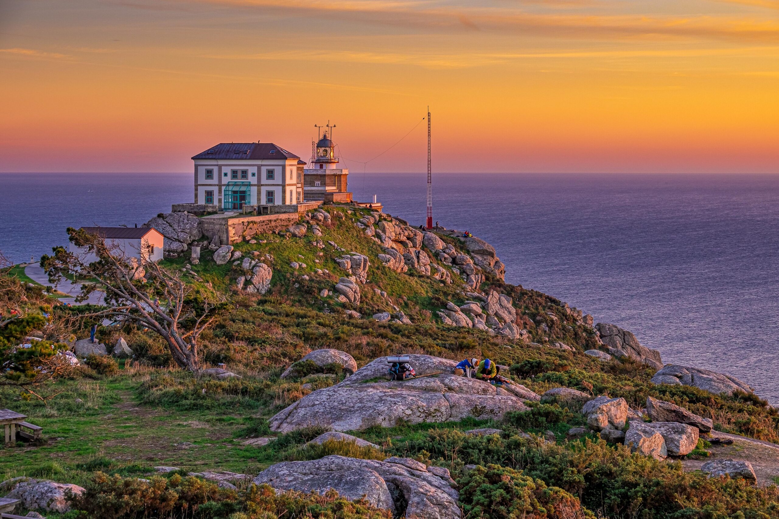 House built on rocky cliff by the sea bathed in sunlight beneath a stormy sky, symbolizing a life built on Jesus Christ