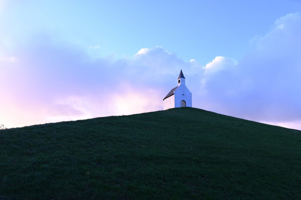Small country church on a hilltop overlooking a lake at sunrise, illustrating the call to seek higher ground with God