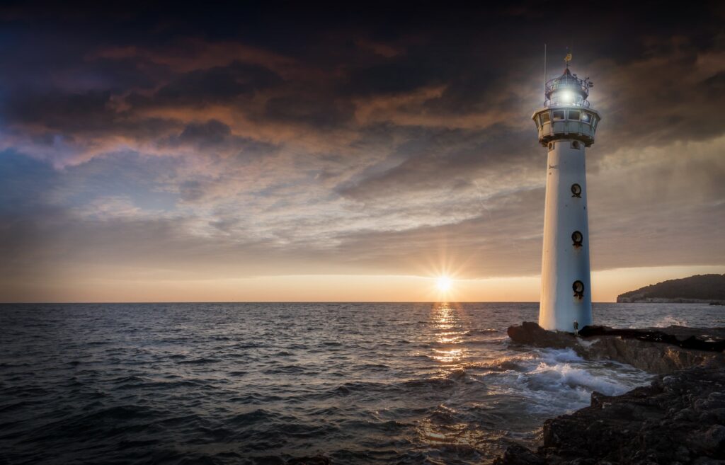 A lighthouse standing firm on a rocky shoreline against crashing waves, illustrating how to stand firm in faith